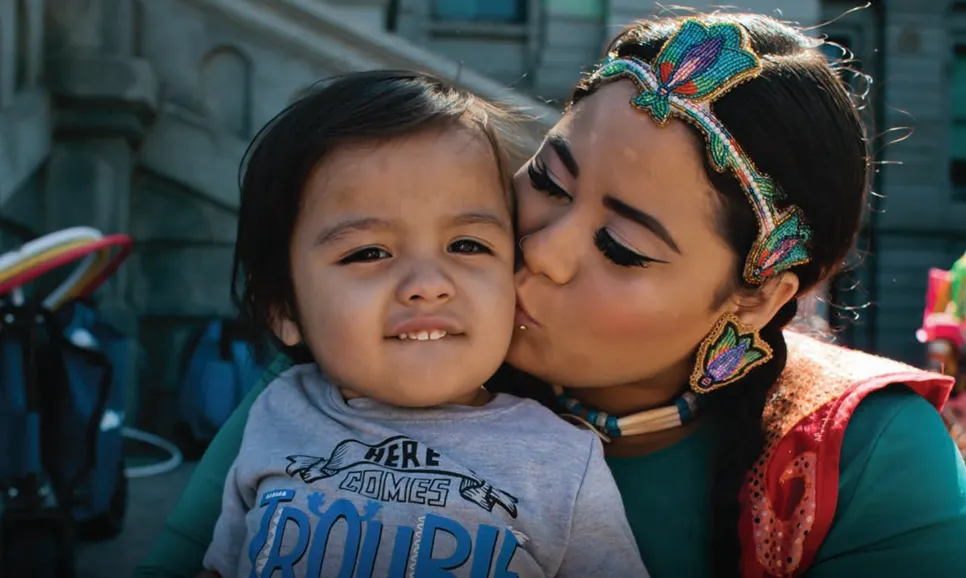 An indigenous mother lovingly kisses her young child on the cheek.